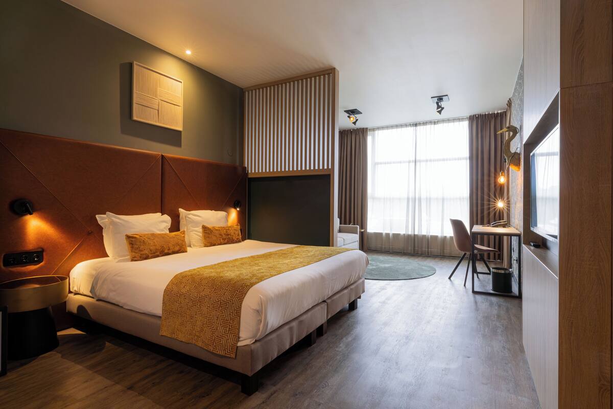 Quarto de hotel moderno com uma cama grande, uma escrivaninha e vista para o exterior.