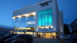 A modern hotel with a glass facade, signage for 'Shanghai Hotel' and 'ENTREE', and a parking lot with several cars. - Shanghai Hotel Holland (Delft)