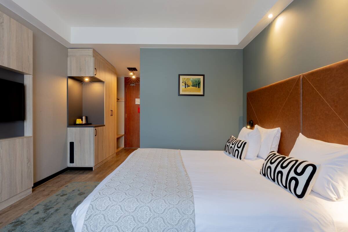Quarto de hotel com uma cama grande, televisão, guarda-roupa e uma pequena cozinha.