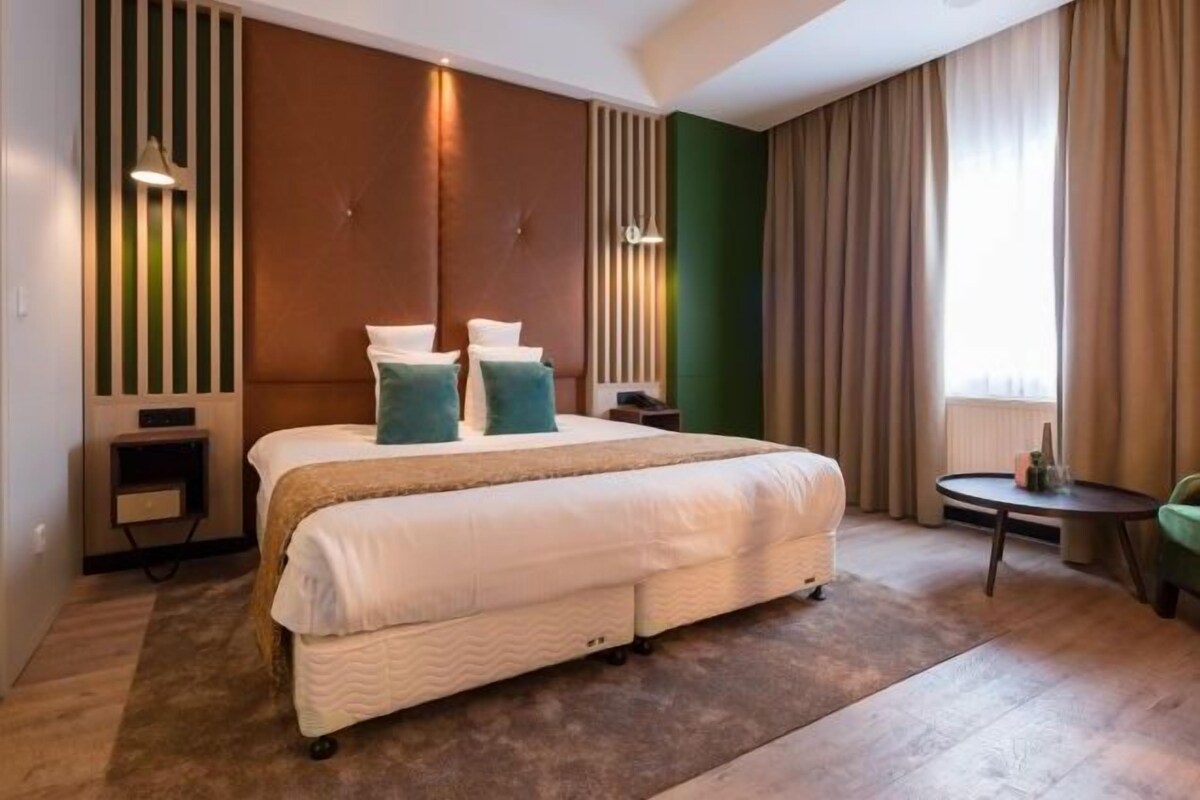 A modern hotel room with a large bed, a small bedside table, a chair, and a round table.