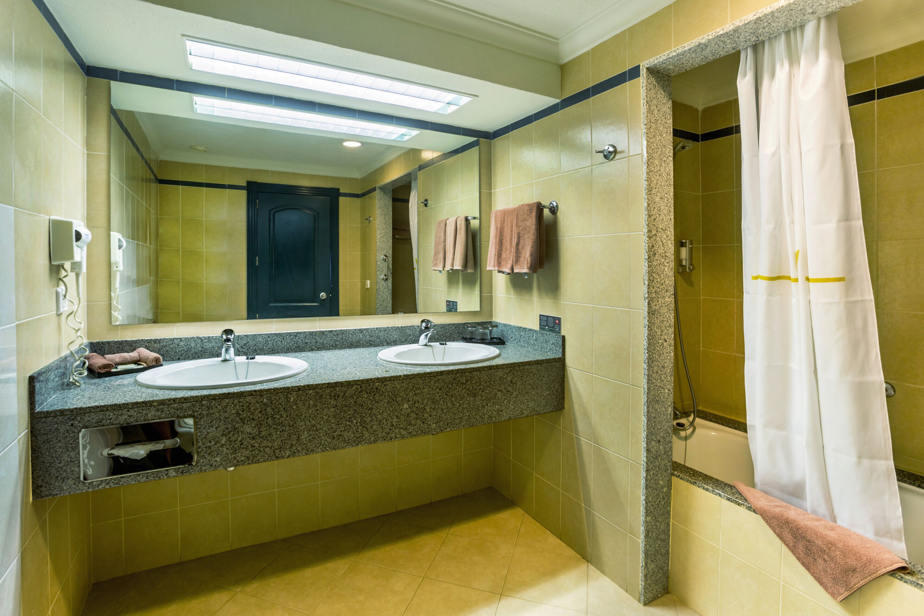 Casa de banho com duas pias, um espelho, chuveiro e porta-toalhas.
