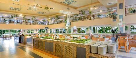 A spacious hotel lobby with a central buffet area, multiple seating arrangements, and a high ceiling with geometric patterns.