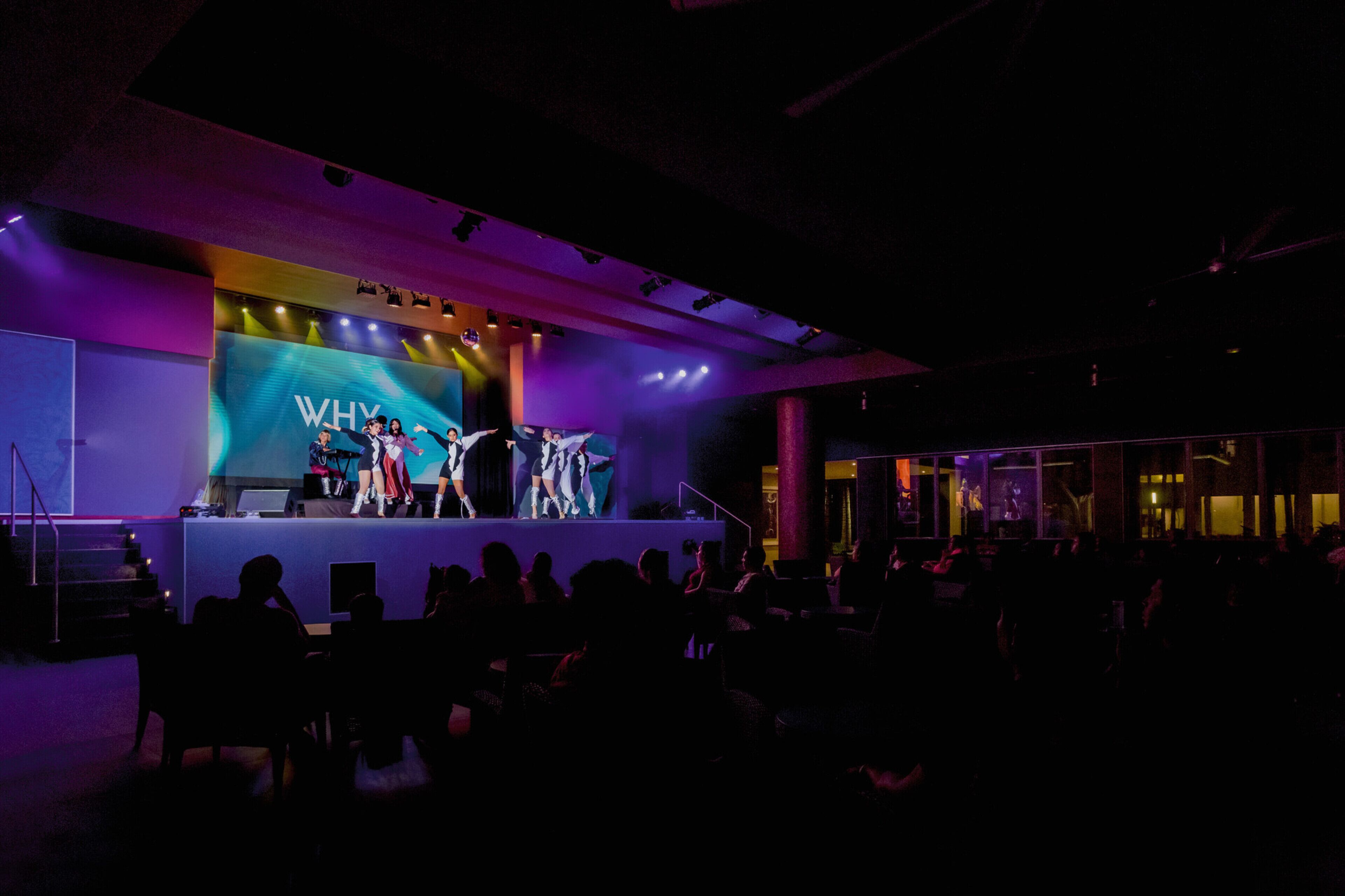 A stage with a backdrop reading "WHY" and a group of people on stage.