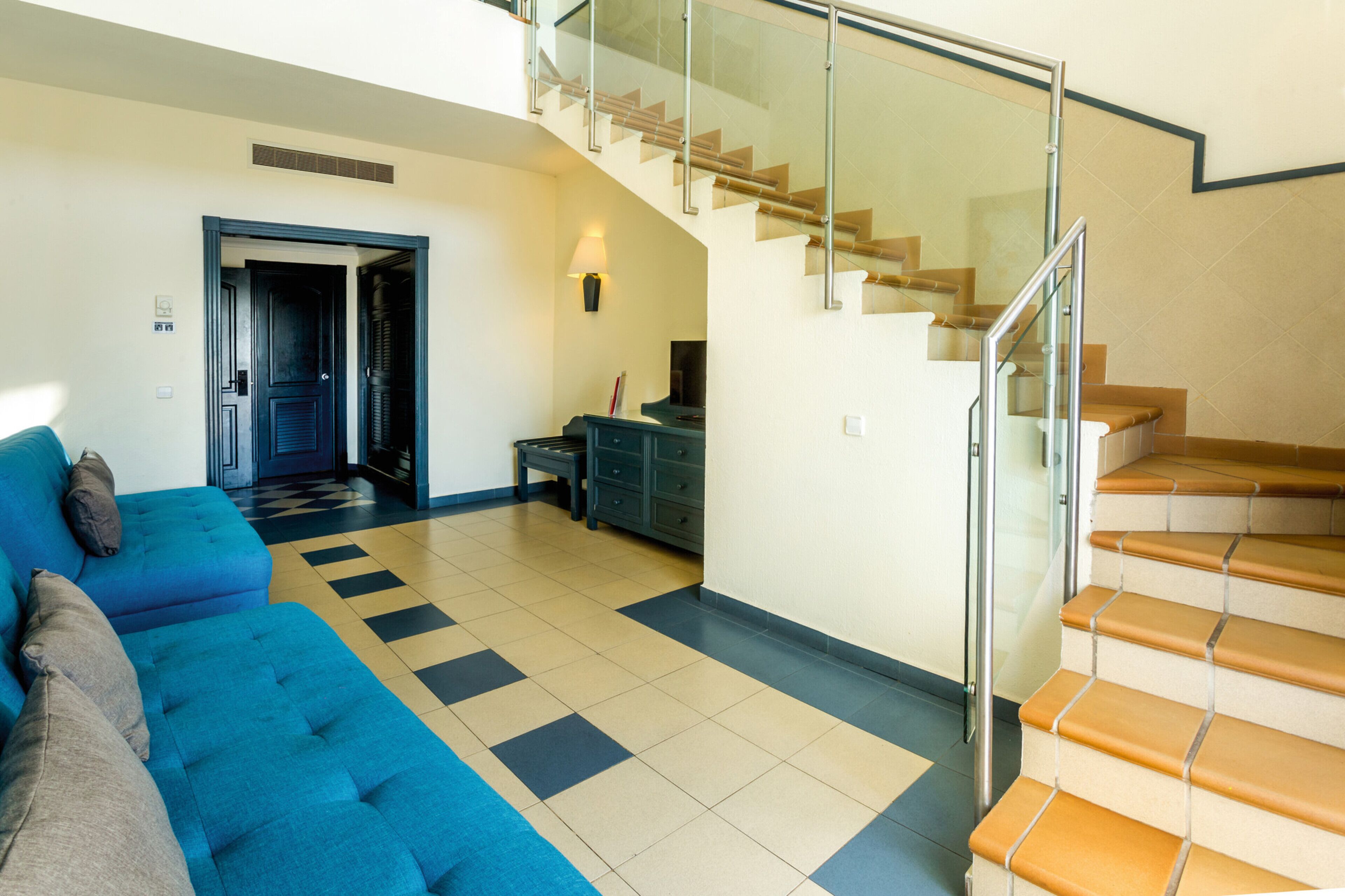 A modern living room with a blue sofa, a staircase, and a dining area.