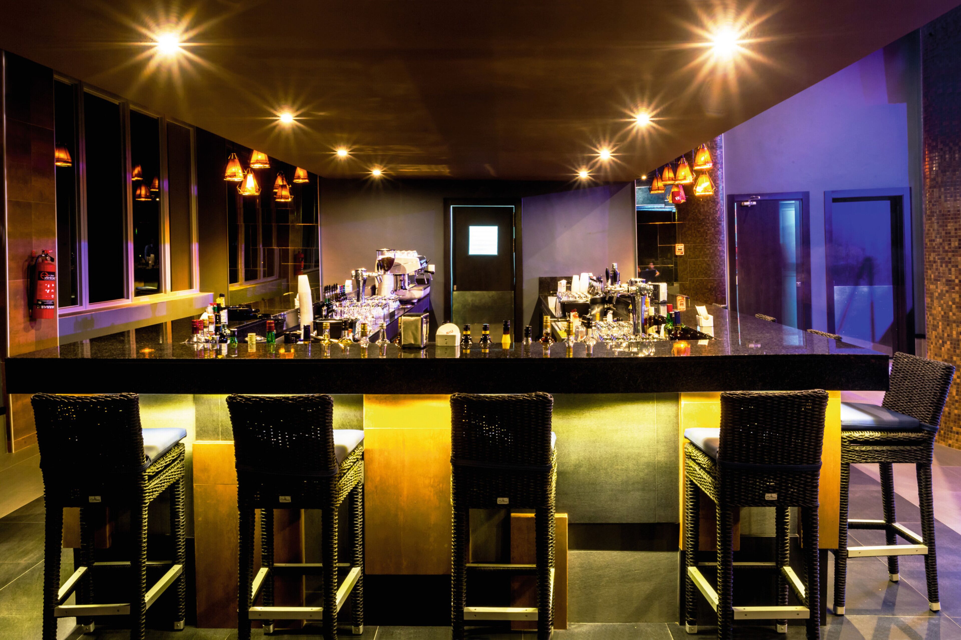 A bar area with a long counter, multiple bar stools, and overhead lighting.
