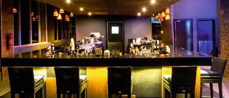 A bar area with a long counter, multiple bar stools, and overhead lighting.