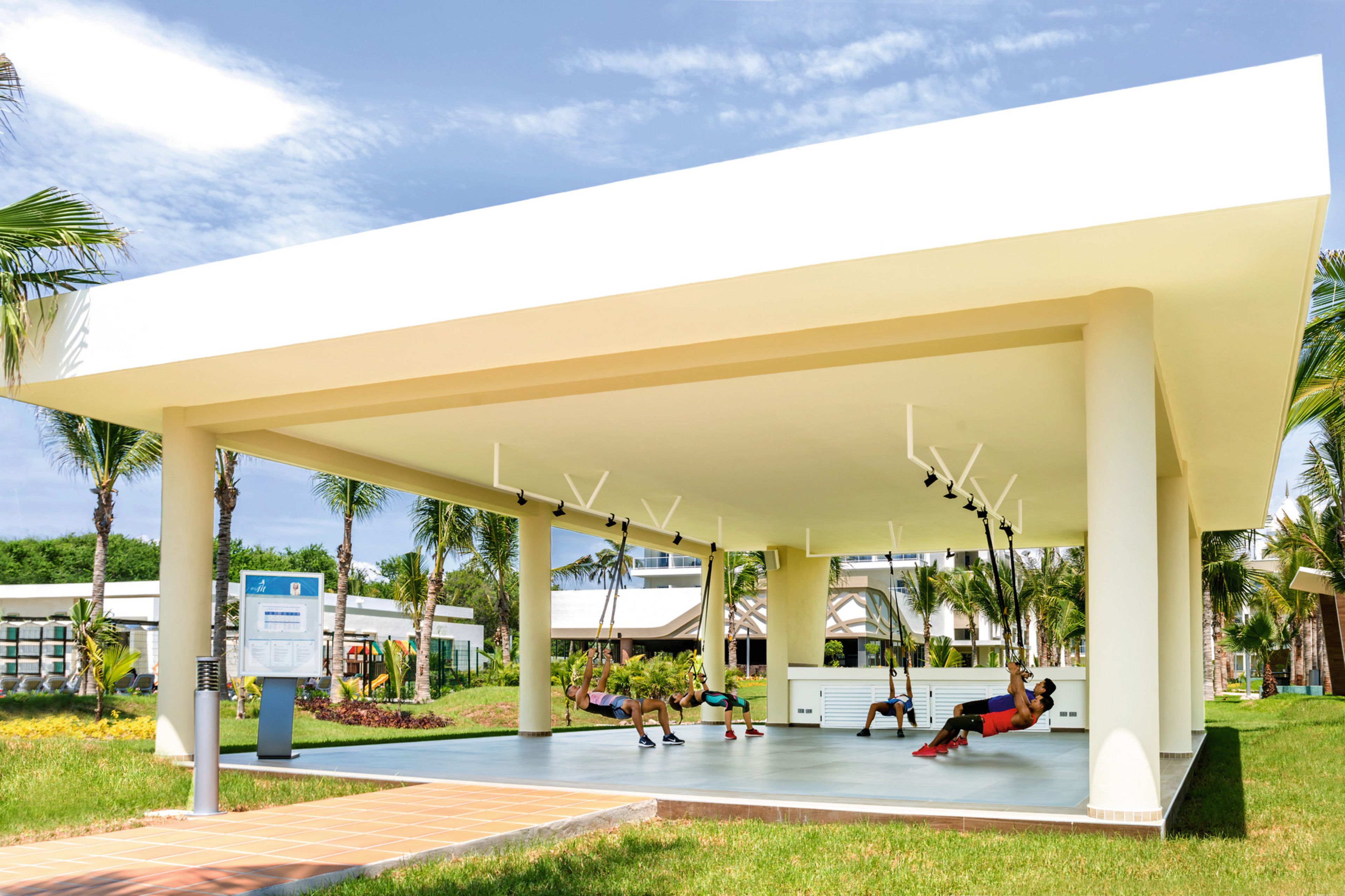 A covered outdoor area with a swing set, palm trees, and a building in the background.