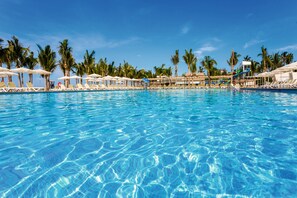 A clear blue pool with lounge chairs and umbrellas, surrounded by palm trees.