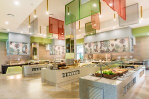 A buffet area with multiple food stations, a central serving counter, and a large window providing natural light.