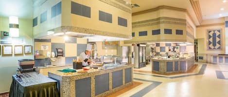 A spacious hotel lobby with a large central kitchen area, multiple service counters, and a clean, tiled floor.