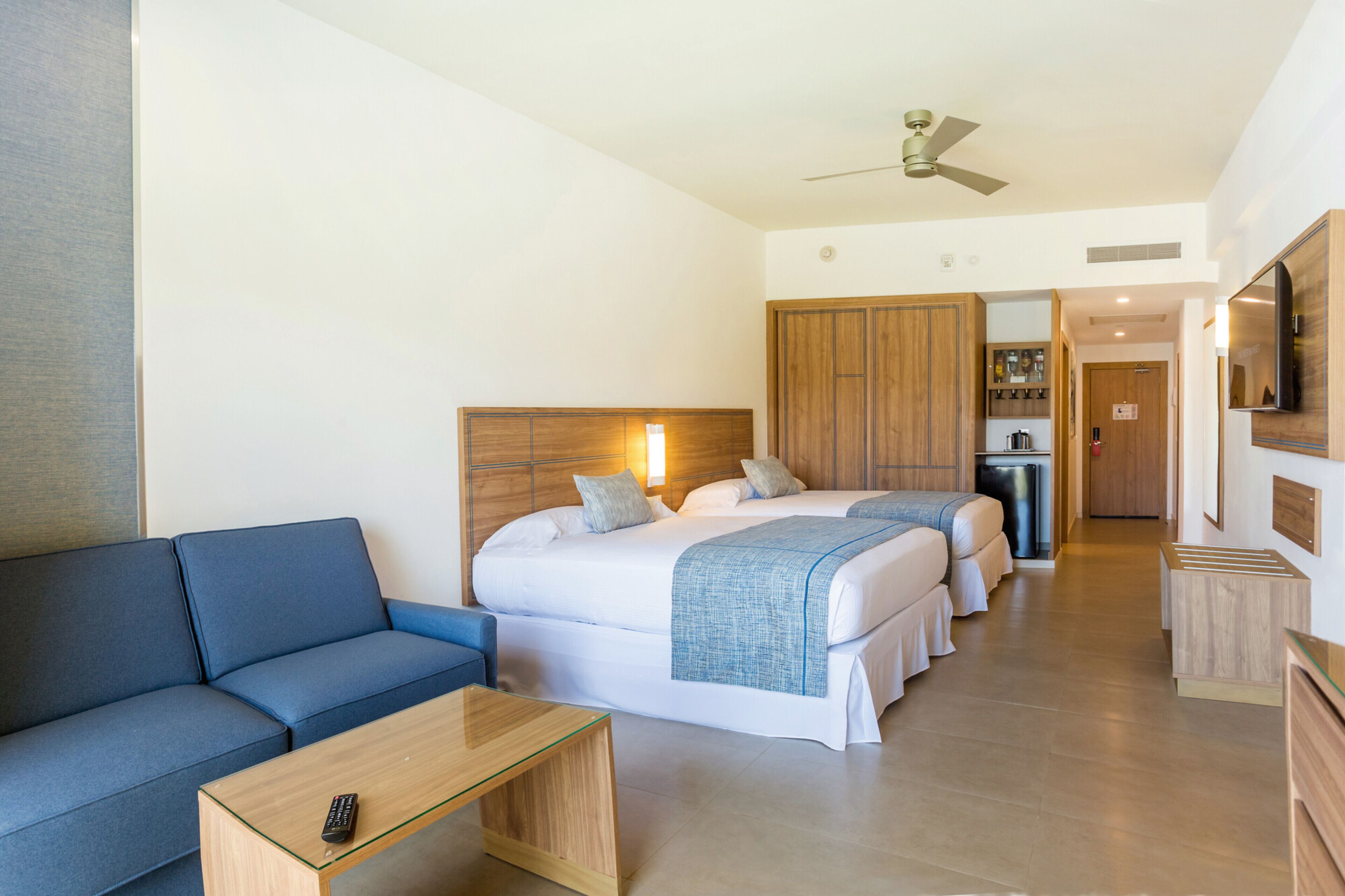 A hotel room with a sofa, two beds, a TV, and a kitchenette.