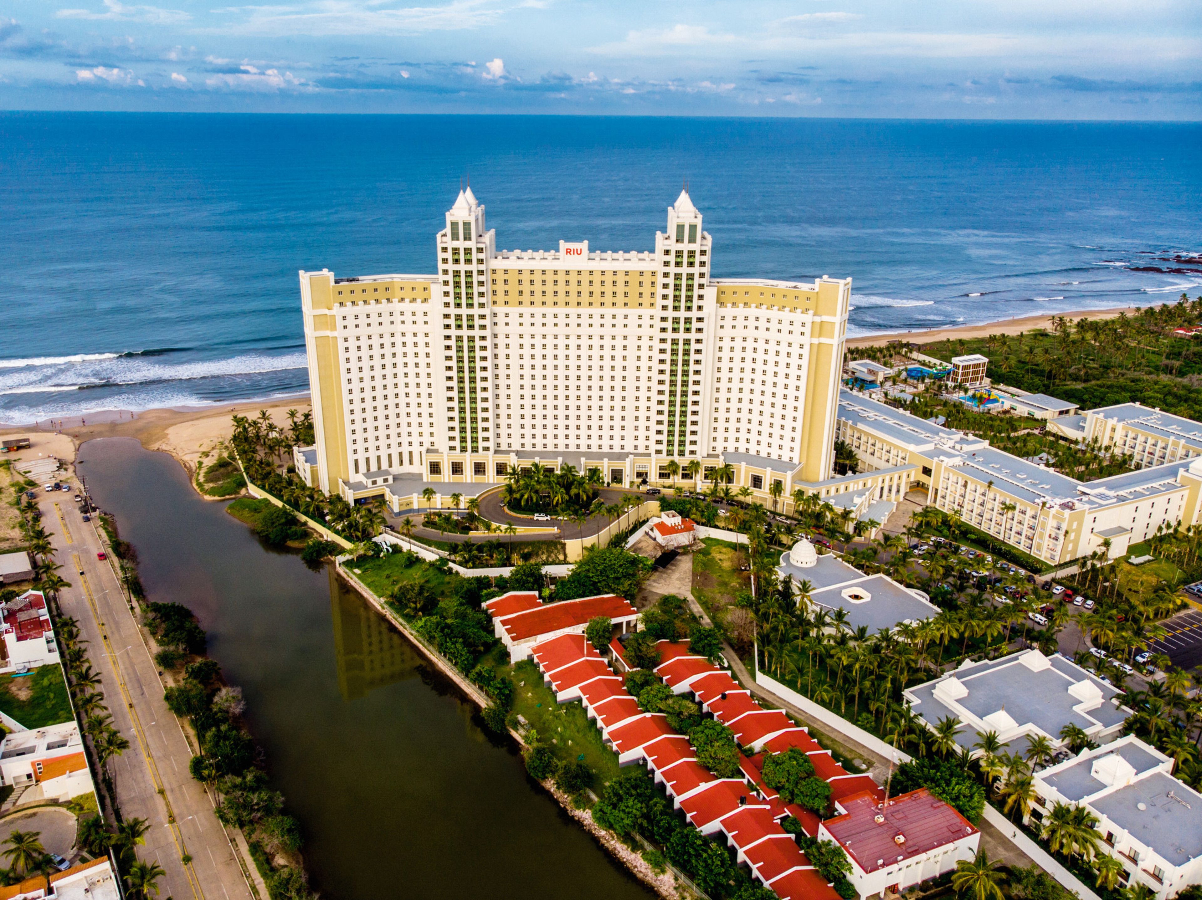 Un gran hotel con varias edificaciones, un río y una playa.