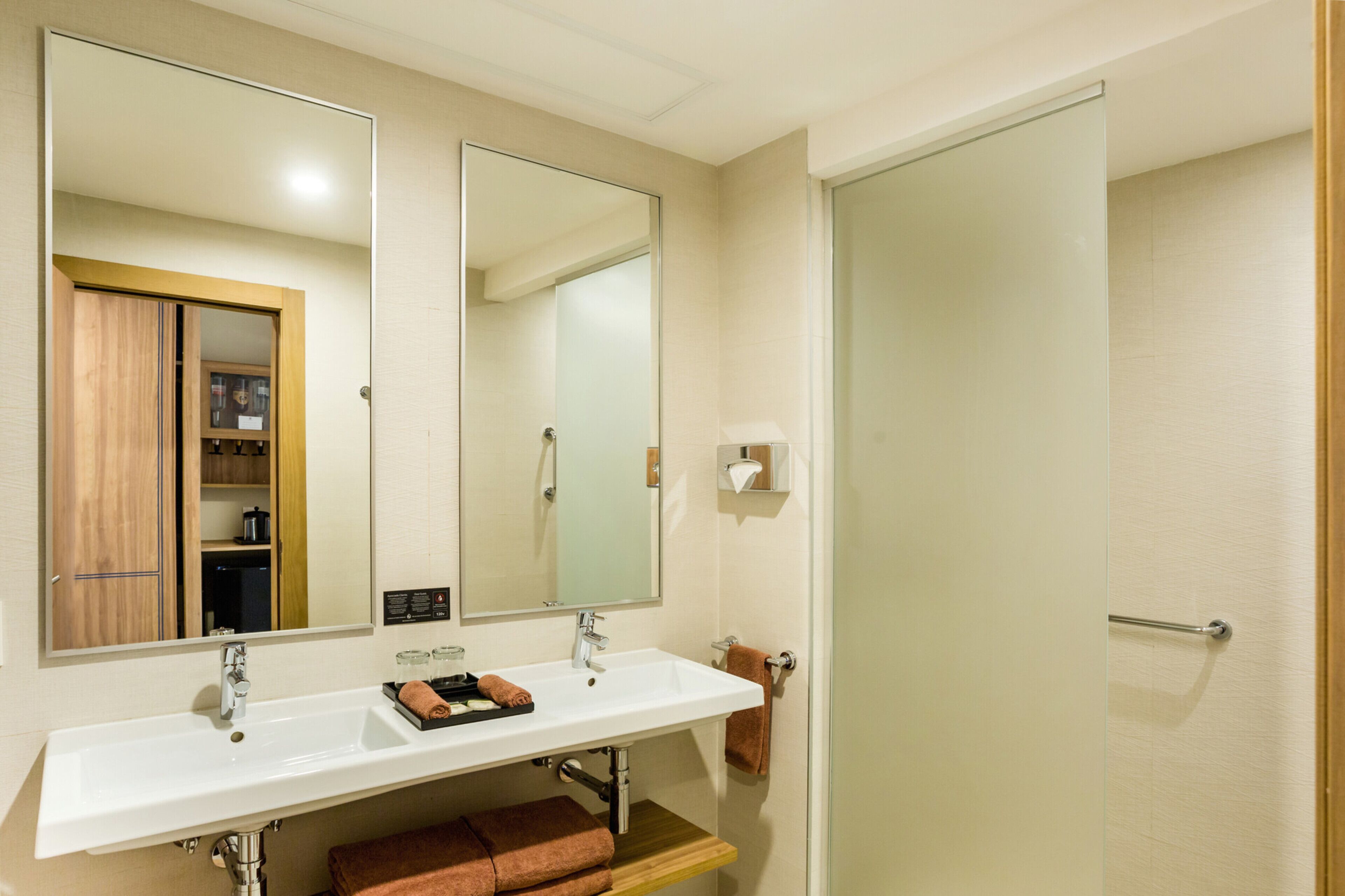 Un bagno con un lavandino bianco, due specchi, un armadietto in legno e un porta asciugamani.