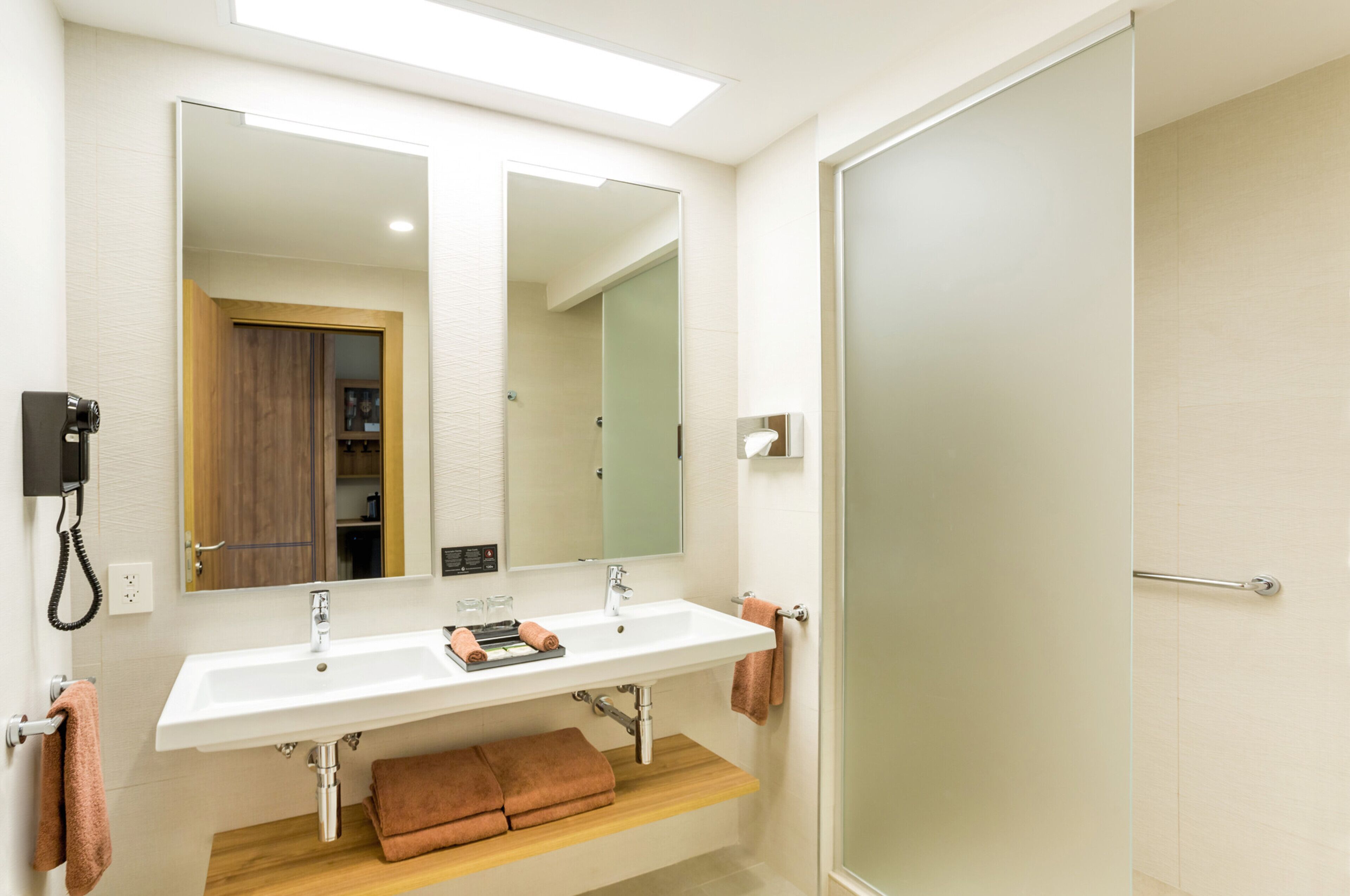 A modern bathroom with a white sink, two mirrors, a wooden shelf, and a towel rack.