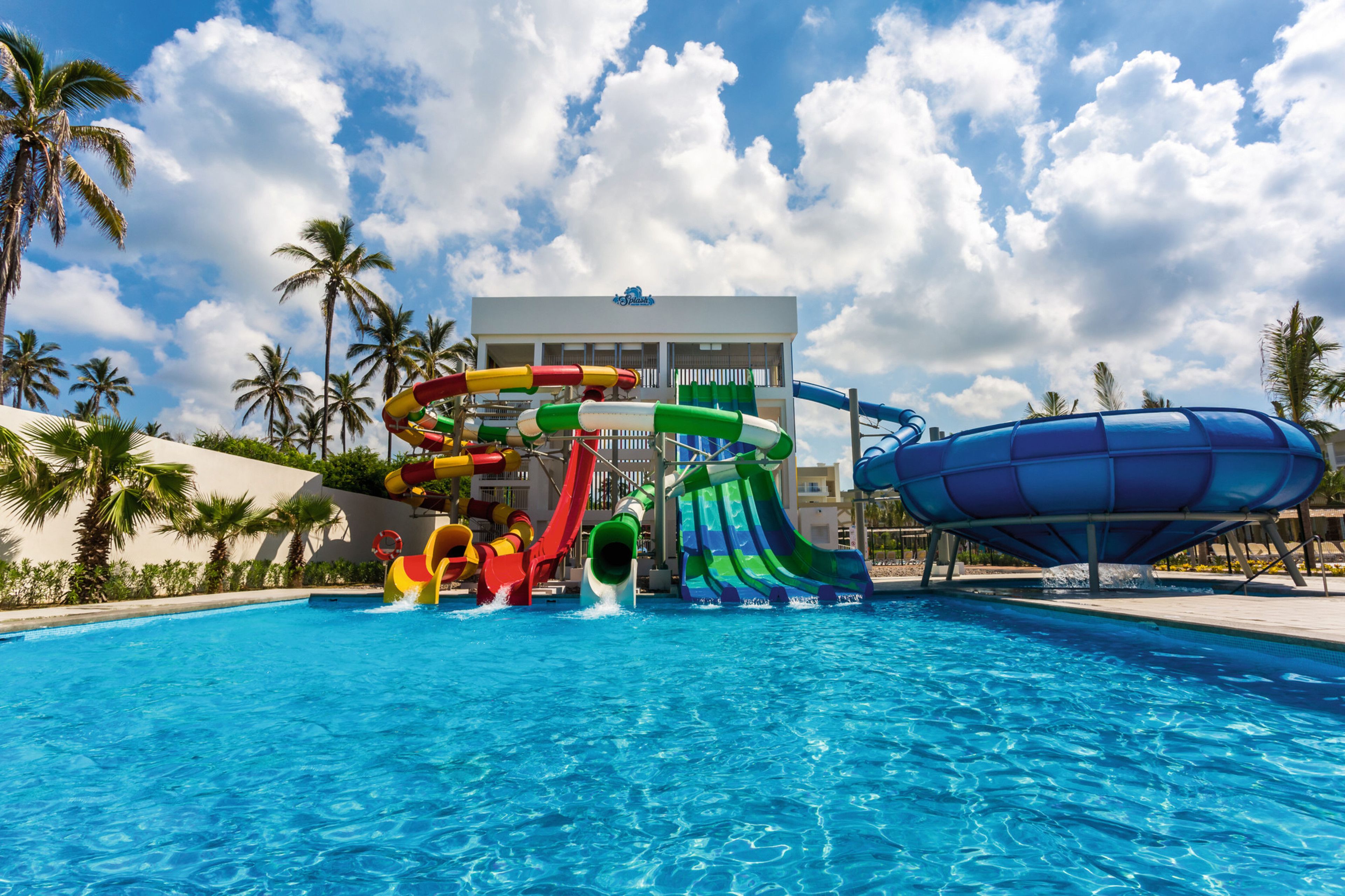 A swimming pool with multiple water slides and a building in the background.