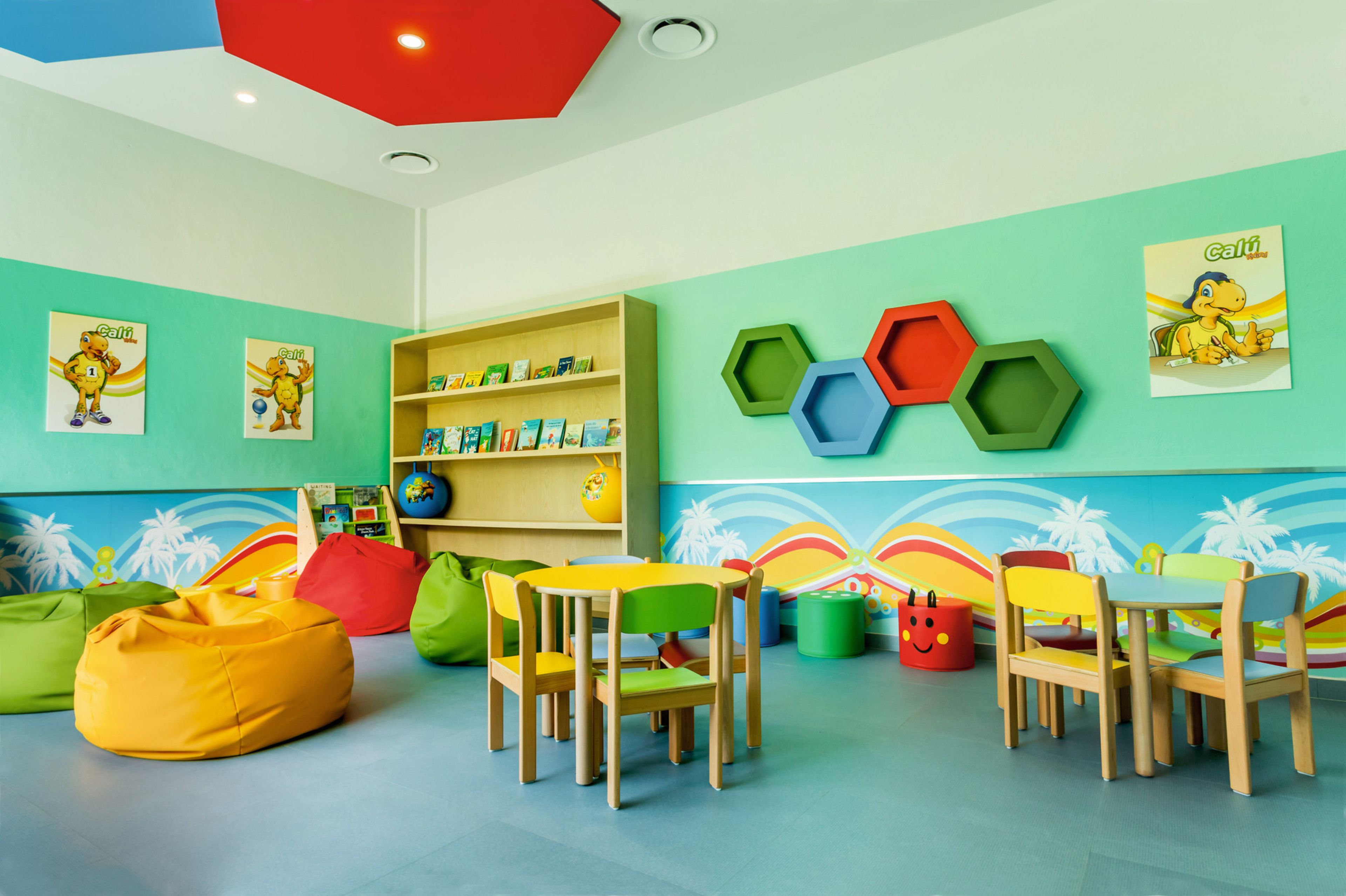 Un cuarto de juegos infantil con muebles coloridos, adornos hexagonales en la pared y estanterías educativas.