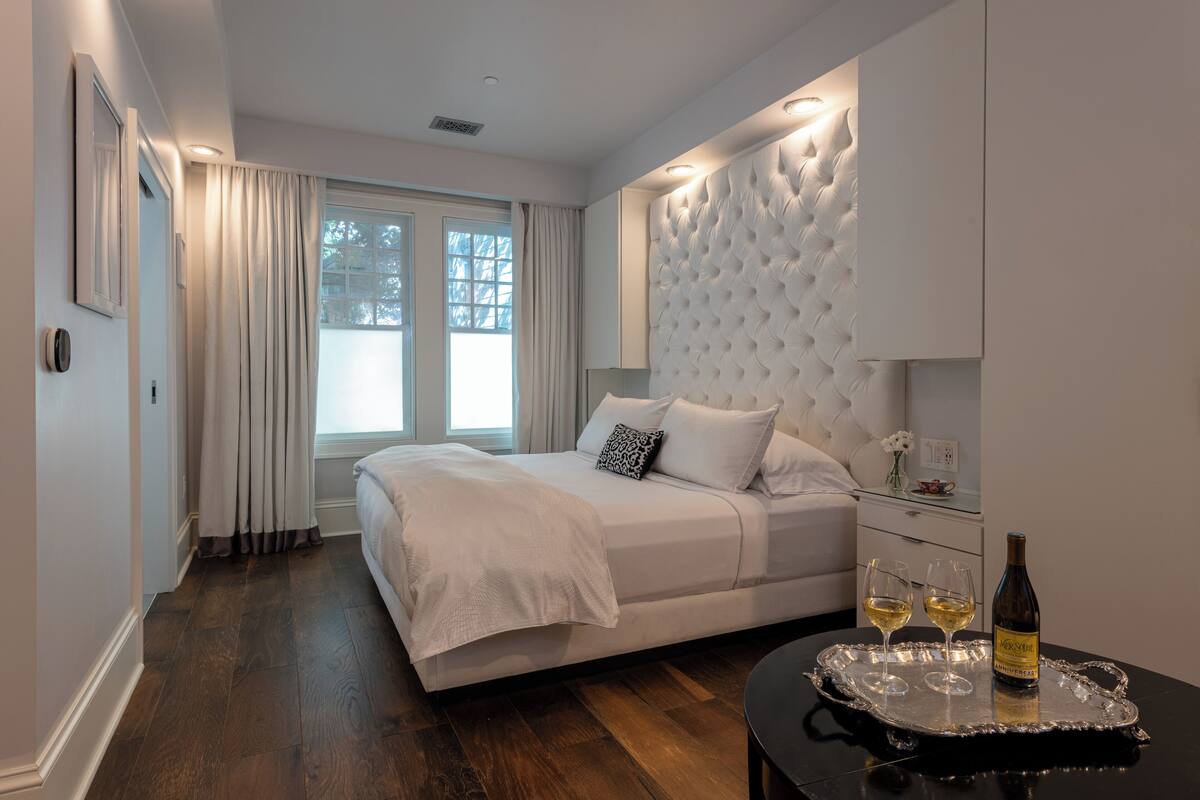 A bedroom with a large bed, a nightstand, and a tray with glasses and a bottle.