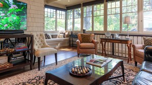 A spacious living room with a large TV, comfortable seating, and large windows offering a view of the outdoors. - Stonehurst Place Bed & Breakfast (Atlanta)