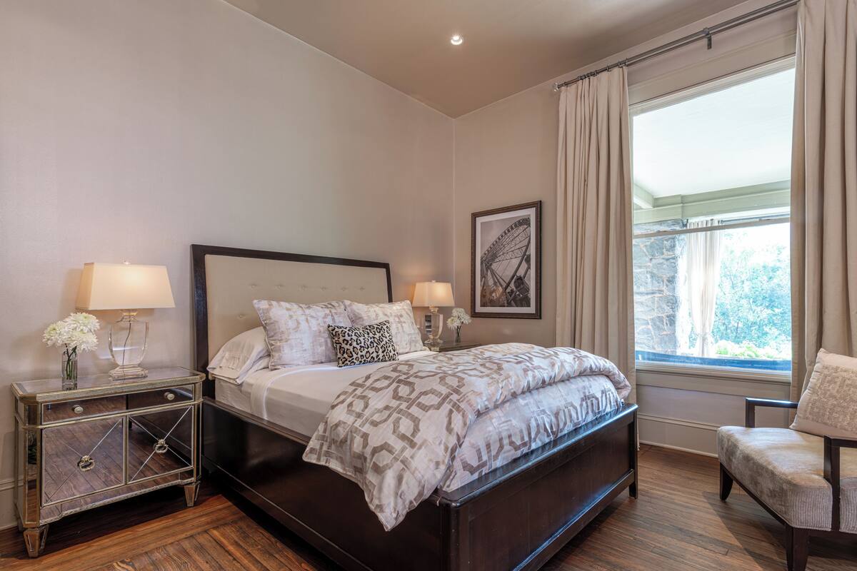 A bedroom with a bed, nightstands, a chair, and a window with curtains.