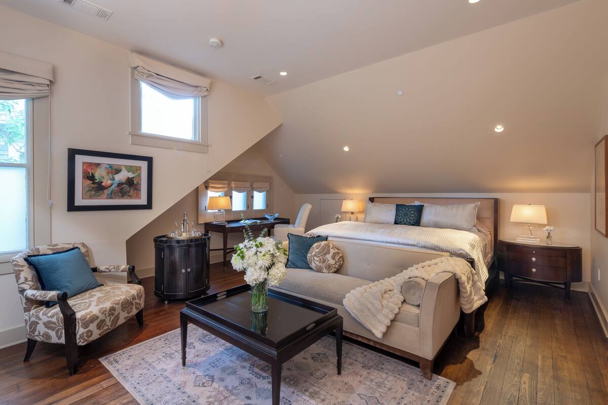 A bedroom with a large bed, a chair, a coffee table, and a nightstand.