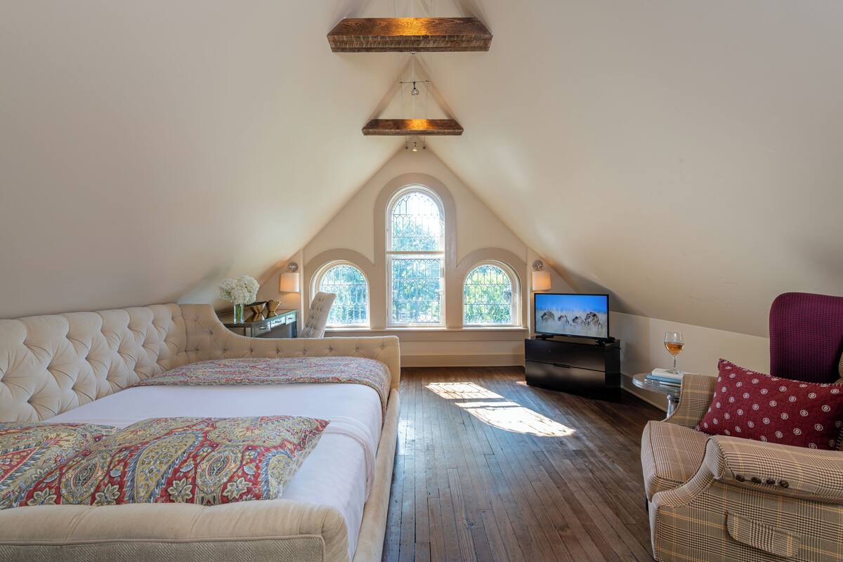 A bedroom with a large bed, a television, and a seating area with a chair and a table.