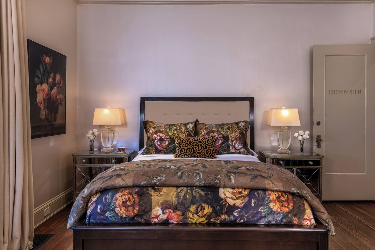 A bedroom with a floral bedspread, two bedside tables with lamps, a headboard, and a door labeled "FARNSWORTH".