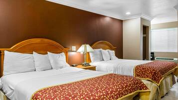 A hotel room with two beds, each with white bedding and a red patterned throw. There is a nightstand with a lamp between the beds.