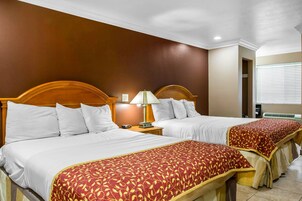 Habitación de hotel con dos camas, cada una con ropa blanca y un plaid rojo estampado. Hay una mesita de noche con una lámpara entre las camas.
