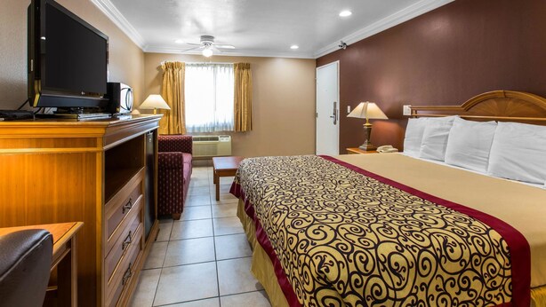 A hotel room with a bed, a desk, a television, and a chair. - Rodeway Inn Cypress - Buena Park (Cypress)