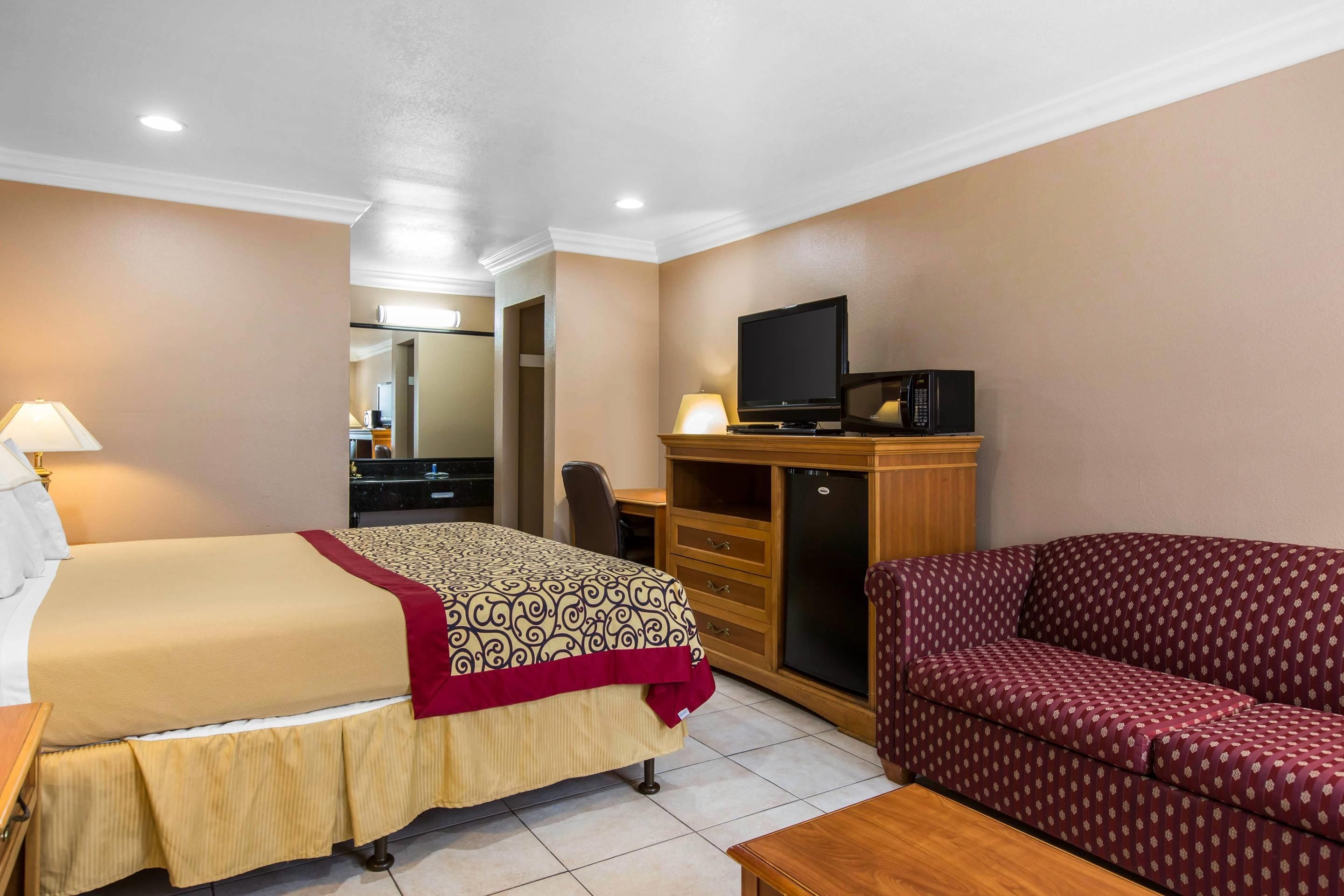 A hotel room with a bed, a sofa, a television, a desk, and a mirror.