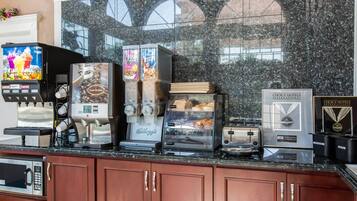 Una estación de café con varias máquinas, incluyendo un dispensador de zumo de fruta, una cafetera, un dispensador de cereales helados, un expositor de pan y un dispensador de mantequilla.