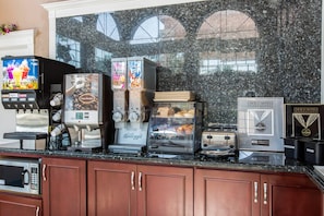 A coffee station with various machines including a fruit juice dispenser, a coffee machine, a frosted cereal dispenser, a bread display, and a butter dispenser. - Rodeway Inn Cypress - Buena Park (Cypress)