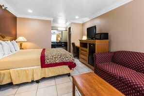 A hotel room with a bed, a sofa, a television, and a desk. - Rodeway Inn Cypress - Buena Park (Cypress)