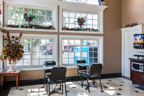 A dining area with a table and chairs, large windows with flower boxes, and a vending machine. - Rodeway Inn Cypress - Buena Park (Cypress)