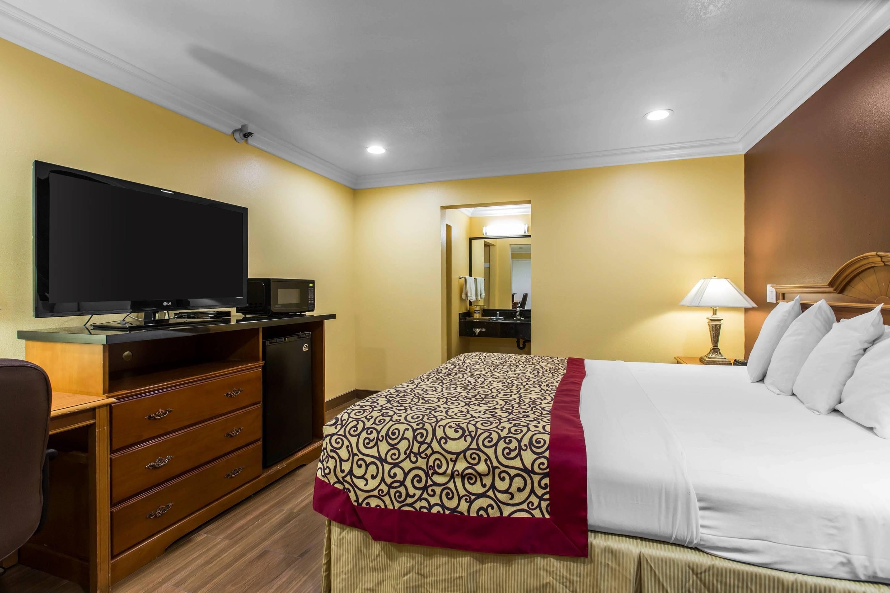 A hotel room with a bed, a television, a desk with a computer, a mirror, and a lamp.