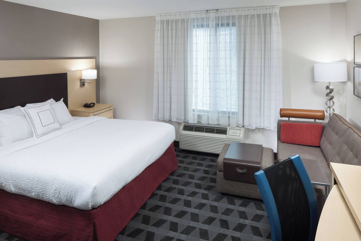 Ein Hotelzimmer mit einem großen Bett, einem Schreibtisch, einem Sessel, einer Couch, einem Nachttisch und einem Fenster mit Vorhängen.
