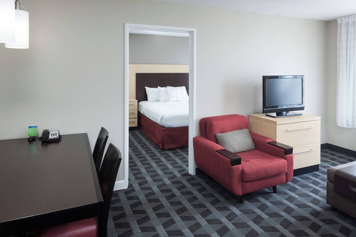 Ein Hotelzimmer mit Bett, Fernseher, rotem Sessel, Schreibtisch und einem gemusterten Teppich.