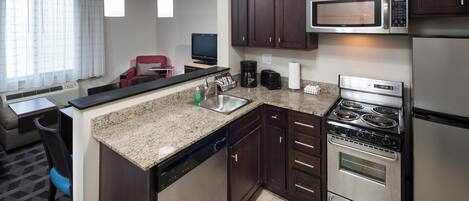 A modern kitchen with a granite countertop, stainless steel appliances, and dark wooden cabinets.