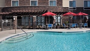 Un espace piscine avec des chaises bleues et des parasols rouges, entouré de murs en pierre et de fenêtres.