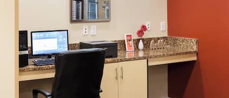 A hotel reception desk with a computer, a chair, and a vase with flowers.