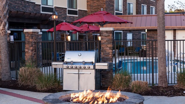Une terrasse extérieure avec un foyer en pierre, un barbecue et des parasols rouges.