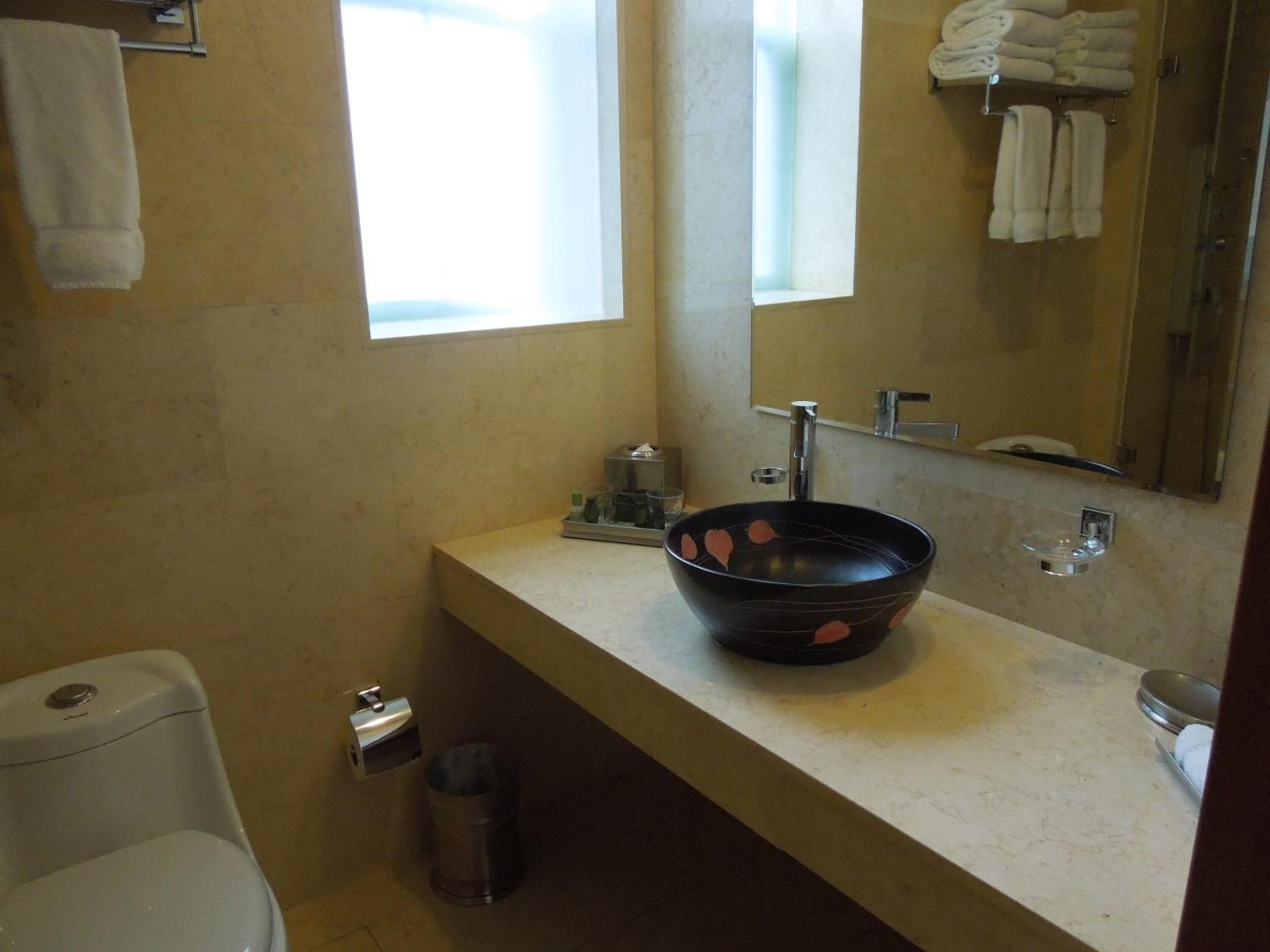 A bathroom with a toilet, a sink with a black basin, a mirror, and a window.