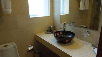 A bathroom with a toilet, a sink with a black basin, a mirror, and a window.