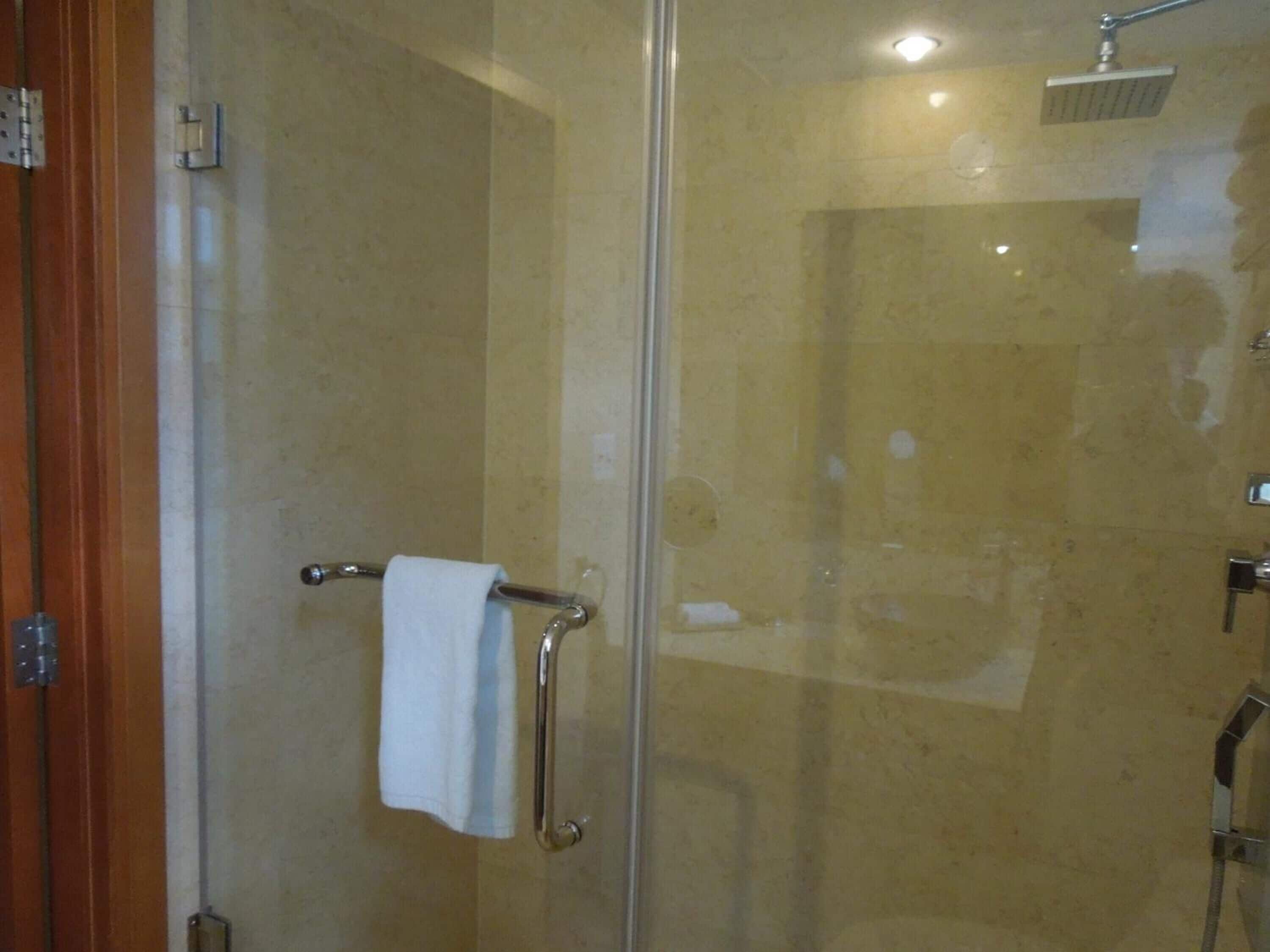 A glass-enclosed shower with a handheld showerhead and a towel rack with a towel.