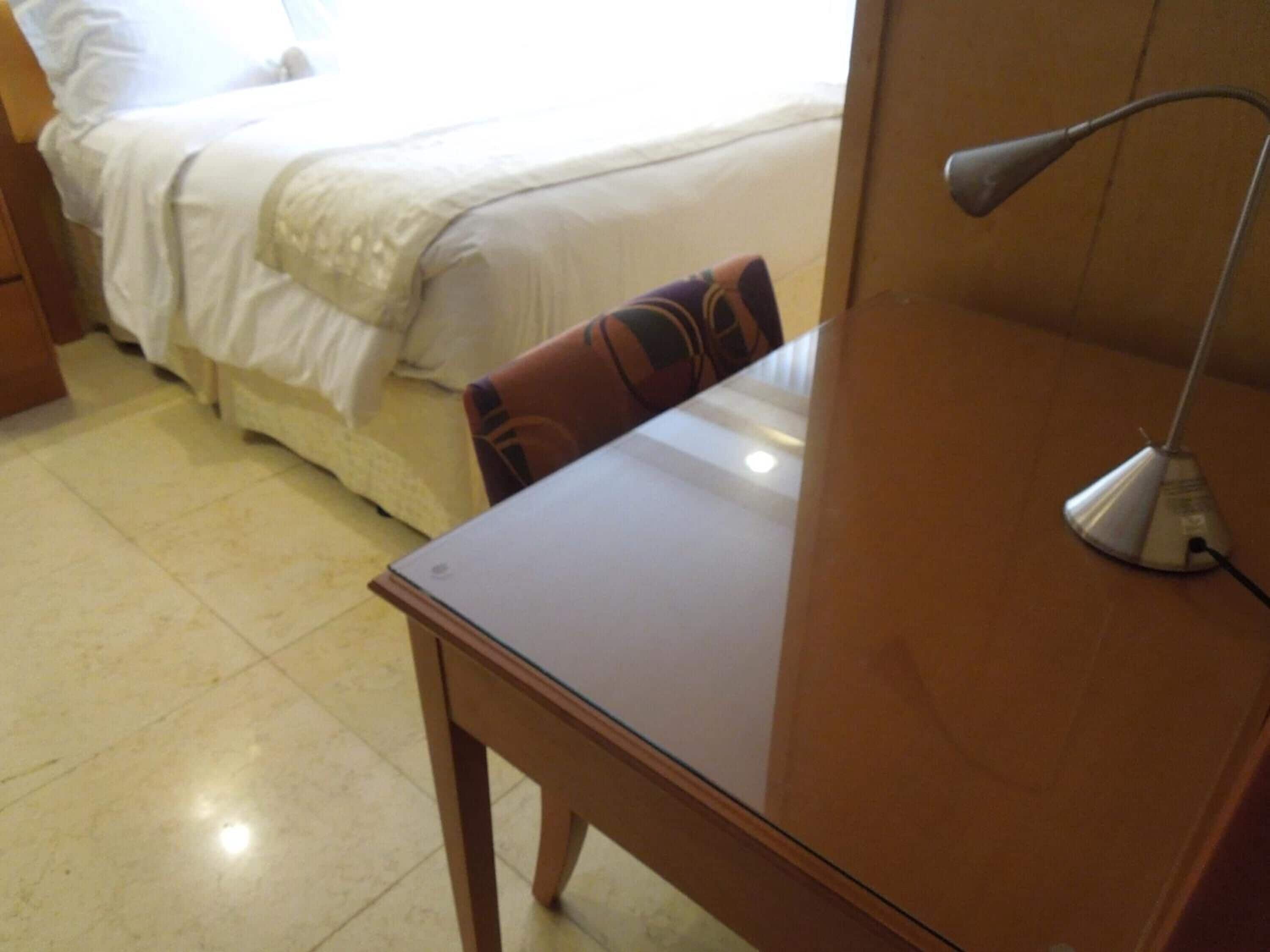 A hotel room with a bed, a wooden table, and a desk lamp.