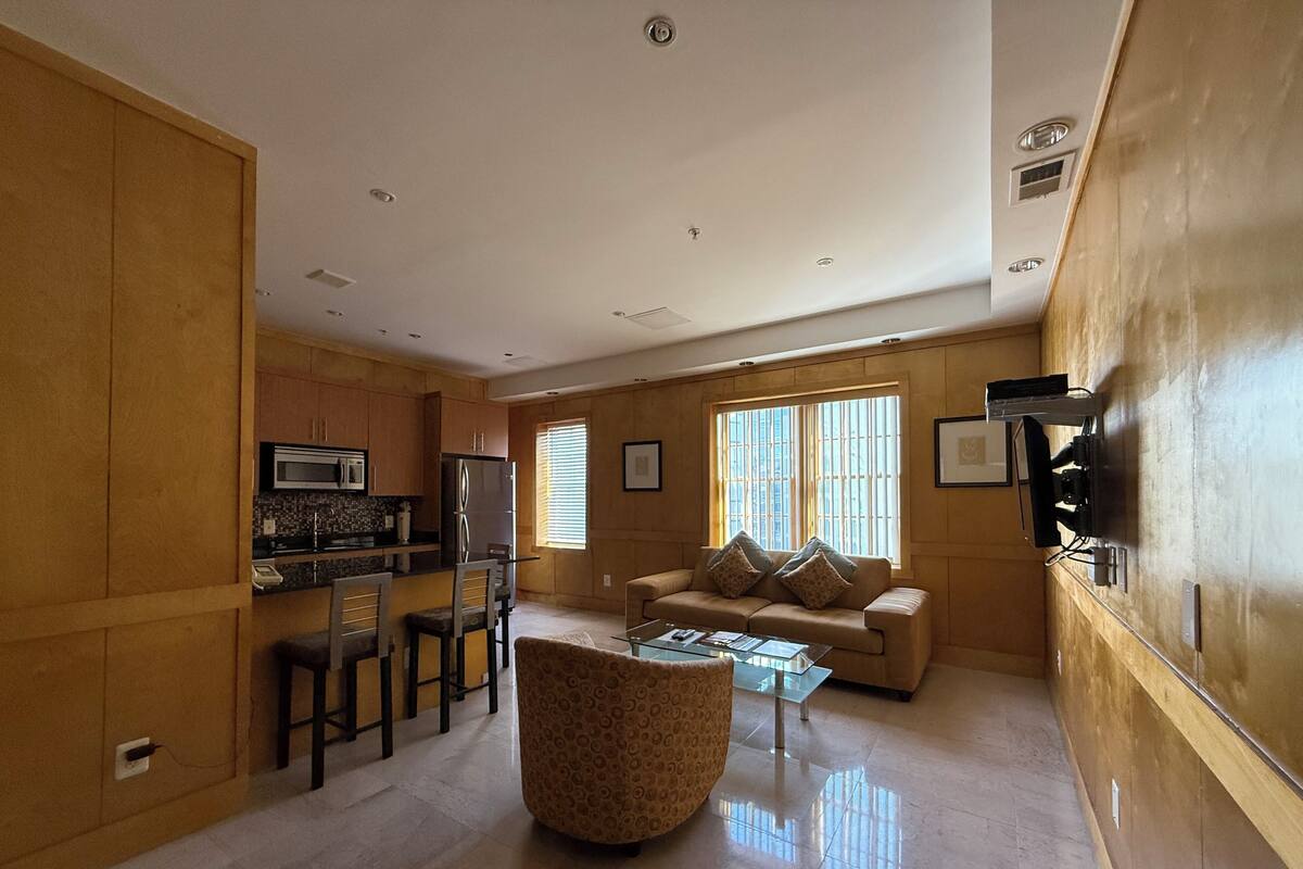 A modern living room with a sofa, coffee table, and kitchen area with wooden cabinets and appliances.