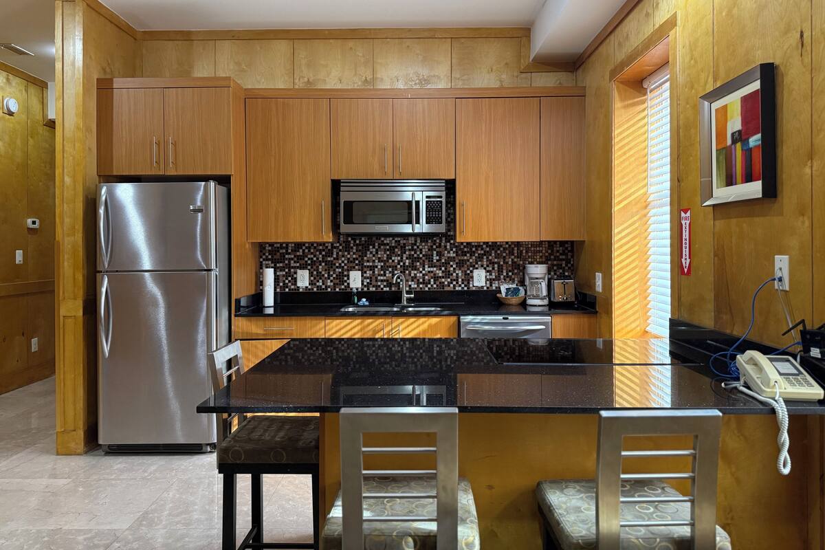 A modern kitchen with wooden cabinets, stainless steel appliances, a black countertop, and a built-in microwave.