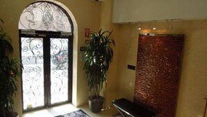 A hotel lobby with a large arched entrance, a reception desk, a potted plant, and a textured wall. - The Eldon Luxury Suites (Washington)