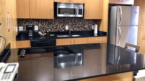 A modern kitchen with wooden cabinets, a black countertop, a stainless steel refrigerator, and a microwave. - The Eldon Luxury Suites (Washington)