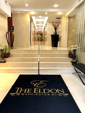 A hotel lobby with a black carpet featuring 'The Eldon Washington DC' logo, marble steps, and a glass door leading to a room. - The Eldon Luxury Suites (Washington)